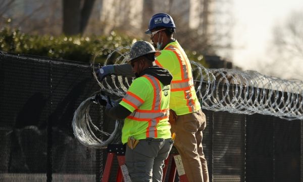 Deux ouvriers installent du fil de rasoir croisé sur le dessus de la clôture.