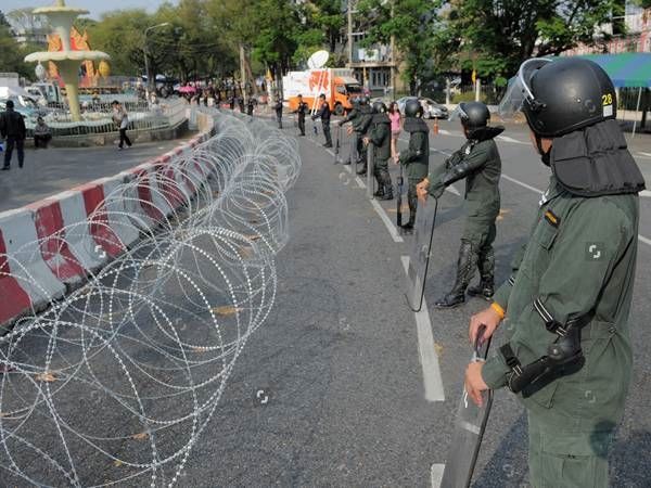 The riot police are standing along mobile razor wire security barrier.