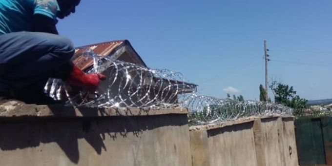 A man is installing razor wire on the topof the wall.